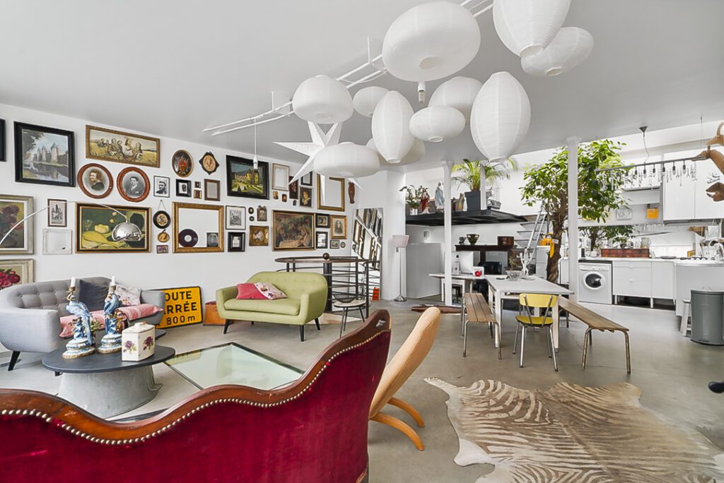 Appartement au design unique à Paris, avec une décoration éclectique de tableaux encadrés, meubles modernes et accessoires colorés. Le salon dispose d'un canapé design, de lampes suspendues originales et d'une table en verre, créant un espace créatif et lumineux.