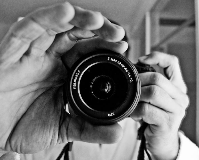 Photo centré sur un objectif d'appareil photo tenu par un photographe, photo en noir et blanc