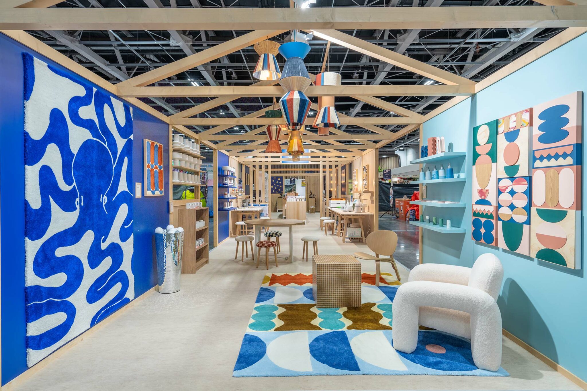 Installation professionnelle colorée et moderne, avec des murs bleus décorés de tapisseries et d'œuvres d'art géométriques. Des meubles design en bois, des chaises minimalistes et un éclairage suspendu créent une atmosphère créative et accueillante.